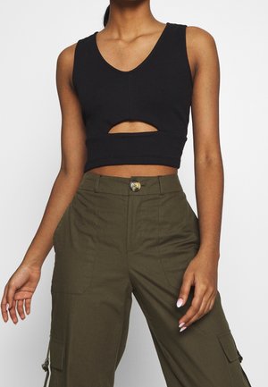 Top court noir à encolure en V profonde et découpe sur le devant, associé à un pantalon cargo vert olive avec poches latérales et fermeture à bouton.
