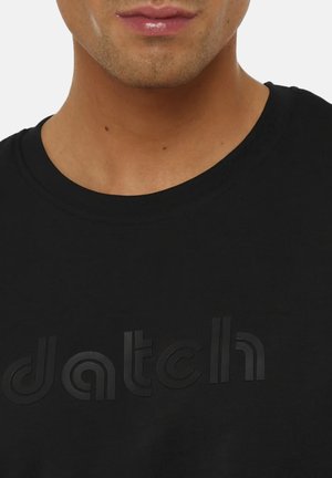 Parte inferiore del volto di una persona che indossa una maglietta nera girocollo con scritta in rilievo "datch" sul petto.