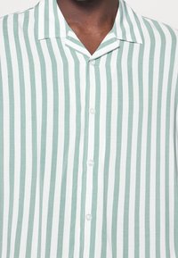 Groen-wit gestreept shirt met korte mouwen, met een kraag, knopen aan de voorkant en een lichtgewicht stof met een zachte textuur. Horizontale strepen.