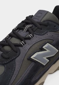Gros plan sur une basket noire et grise avec des lacets noirs et un grand logo réfléchissant en forme de lettre N sur le côté.