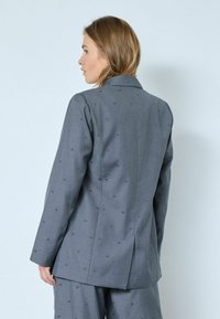 Blazer gris ajustado con un sutil patrón de puntos, abertura simple en la parte posterior y solapas clásicas. Hecho de una tela texturizada para mayor estructura.