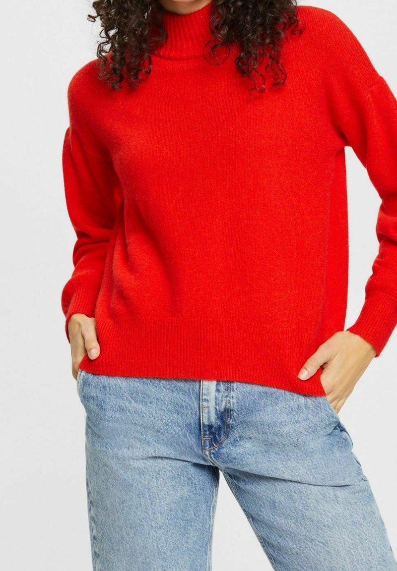 Roter Rollkragenpullover aus Wolle mit lockerer Passform, gerippten Bündchen und Saum, kombiniert mit hellblauen Denim-Jeans.