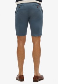 Pantaloni corti da uomo in cotone blu con tasche laterali e posteriori. Tessuto liscio, vestibilità sagomata e dettagli rossi a contrasto sui lembi delle tasche.
