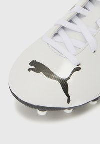 Fehér focicipő texturált felsőrésszel és fekete Puma logóval. Fehér fűzőkkel és formázott stoplival rendelkezik a tapadás érdekében.