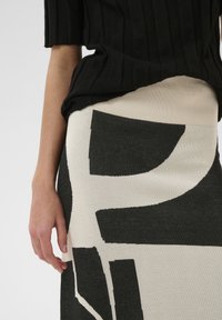 Schwarzer Rippsweater mit kurzen Ärmeln, kombiniert mit einem weißen und schwarzen Strickrock mit abstrakten Mustern und einem taillierten Bund.