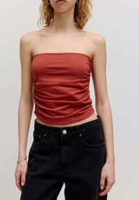 Rostfarbene, trägerlose Bluse mit geraffter Textur, kombiniert mit hochgeschnittenen schwarzen Jeans aus Denim, die über fünf Taschen und einen Metallknopf verfügen.