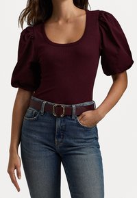Burgundy puffärmad bodysuit i ribbat tyg, kombinerad med högmidjade blå denimjeans, säkrad med ett brunt bälte med en guldbuckle.