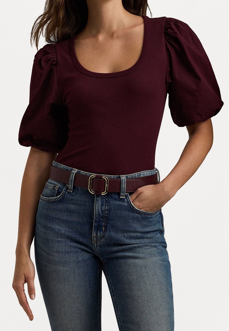 Burgundy puffärmad bodysuit i ribbat tyg, kombinerad med högmidjade blå denimjeans, säkrad med ett brunt bälte med en guldbuckle.