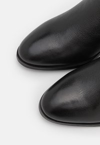 Botas de tobillo de cuero negro con un acabado texturizado, diseño de punta afilada y un contorno elegante y minimalista. Suela de goma para mayor durabilidad.