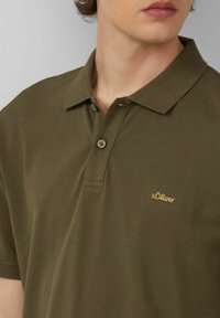 Dunkelgrünes Polohemd aus strukturiertem Stoff, mit klassischem Kragen, zwei Knöpfen und einem goldenen bestickten Logo auf der Brust.