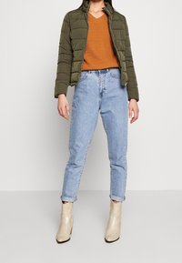 Olivengrøn dunjakke, orange tekstureret striktrøje, lyseblå højtaljede jeans og beige ankelstøvler med slangeskindsprint.