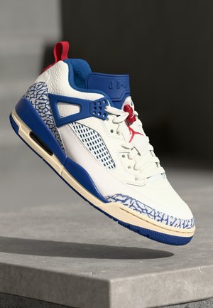 Hvid og blå high-top sneaker med røde accenter, elefantprint og "JORDAN" branding på tungen, vist over en stenoverflade.