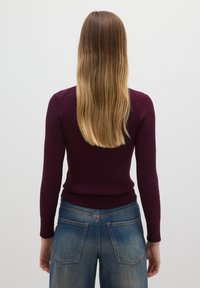 Maglione bordeaux a coste con maniche lunghe abbinato a jeans blu slavato a vita alta, con tasche posteriori e vestibilità ampia.