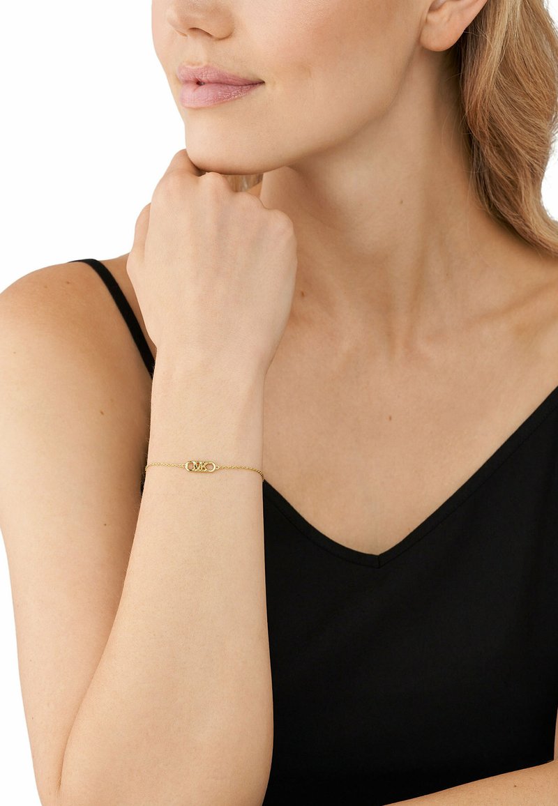 Bracciale in oro con chiusura ovale, indossato su un polso, caratterizzato da un design minimalista e una texture fine su una maglietta scura.