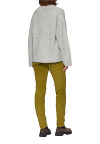 Grijze gebreide trui, gele corduroy broek en bruine enkelboots. De trui heeft een losse pasvorm; de broek is slank en gestructureerd.