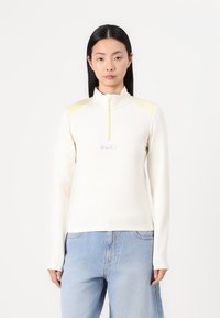 Langermet, glidelås topp i off-white med gule skulderaksenter, med en teksturert overflate og "ROXY"-logo i lys blått på brystet.