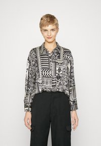 Black and white patterned shirt with long sleeves, button-down collar, and intricate geometric and floral designs. Paired with black trousers.