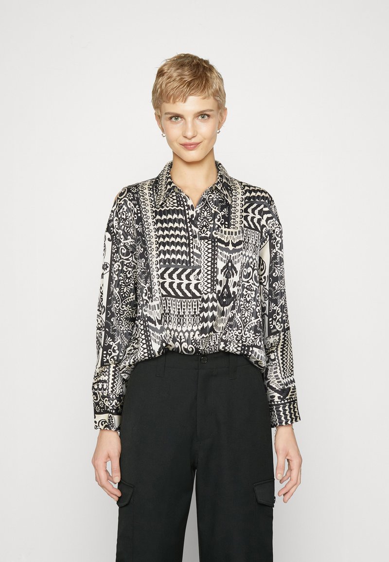 Black and white patterned shirt with long sleeves, button-down collar, and intricate geometric and floral designs. Paired with black trousers.