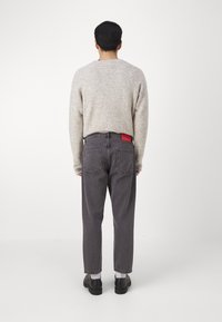 Jeans en denim gris avec une coupe décontractée et des coutures visibles, dotés d'une étiquette de marque rouge sur la poche arrière, portés avec un pull léger.