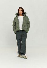 Puffer jacket in olive green with a hood, zip closure, and quilted design; paired with dark tapered pants and light hiking shoes.
