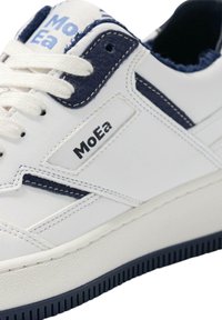 Witte leren sneaker met marineblauwe accenten, voorzien van een gestikt ontwerp, ronde neus, gestructureerde zool en 'MoEa'-branding op de zijkant.