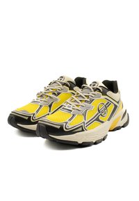 Scarpe da ginnastica con una tomaia in rete prevalentemente gialla, accenti grigi e neri, suole spesse e dettagli riflettenti sui lati e sulla punta.