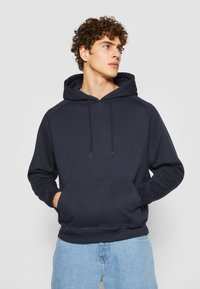 Felpa blu navy realizzata in tessuto morbido, con tasca frontale, cappuccio regolabile con cordino e polsini e orlo a costine.