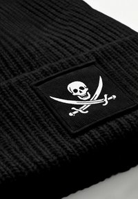 Black knitted beanie with a ribbed texture, featuring a white skull and crossed swords logo on a rectangular patch.