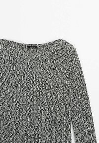 Gestreifter Pullover in Schwarz und Weiß, mit weitem Ausschnitt, langen Ärmeln und einem strukturierten Muster in lockerer Passform. Etikett am Nacken sichtbar.