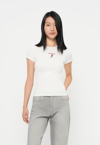 T-shirt blanche ajustée à manches courtes avec une rose rouge brodée et le texte "tommy". Porté avec un pantalon en denim gris clair.