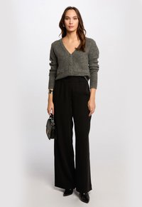 Gray, textured cardigan with a V-neck, two front pockets, and three buttons, paired with black, loose-fitting trousers and black heels.