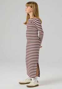 Długa sukienka w paski z poziomymi bordowymi i białymi paskami, z bocznym rozcięciem, o prążkowanej fakturze, zestawiona z białymi skarpetkami i jasnymi sneakersami.