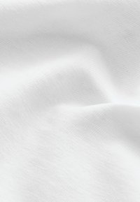 Gros plan d'un tissu blanc doux montrant une texture fine et des plis subtils.
