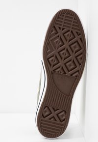 Brown rubber sole of a sneaker with a geometric pattern; features white sidewalls and a logo with a star. Upper part is not visible.