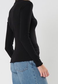 Schwarzes Langarmtop mit gerippter Textur, geschwungener Saum und gerafften Manschetten, kombiniert mit hellblauen Jeans.