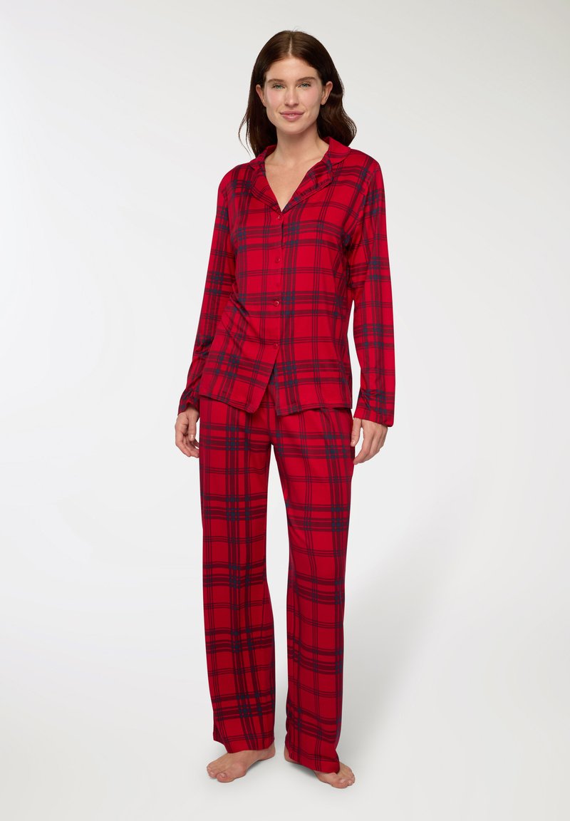Completo pigiama a quadri rossi realizzato in tessuto morbido; presenta maniche lunghe, camicia con bottoni e pantaloni larghi abbinati con dettagli scuri.
