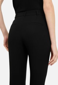 Schwarze Hose mit taillierter Passform, glatter Textur, zwei Gesäßtaschen und einem eleganten Design, mit einem mittelhohen Bund.