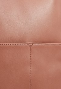 Panel z broskvového kůže s hladkým povrchem, zdobený pečlivým švem a jemným leskem, který zvýrazňuje spojení mezi dvěma sekcemi.