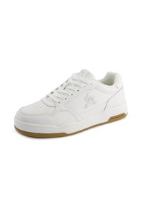 Hvide sneakers lavet af glat læder med en perforeret tåboks, flade snørebånd og en brun gummi sål. Har et logo på siden.