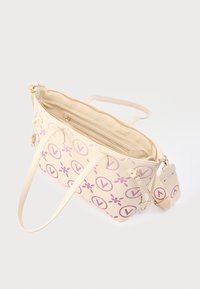 Kremna torbica za na rame z roza okroglim V in cvetličnimi vzorci, dvema naramnima trakovoma, odstranljivim širokim trakom in odprtim zadrgo, ki razkriva notranji žep.