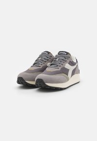 Sneaker grigie in suede con un emblema bianco, dettagli testurizzati e una soletta imbottita. Presentano lacci grigi e accenti di cucitura gialla.