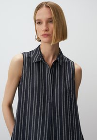 Blusa senza maniche di colore blu navy con righe bianche verticali, design con colletto, tessuto leggero e chiusura a bottoni discreta sul davanti.