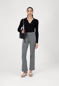 Zwarte geribbelde langemouwen top met V-hals, broeken met ruitpatroon en uitlopende pijpen, zwarte handtas en beige hoge hakken. Eenvoudige ontwerpelementen.