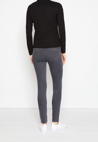 Top negro de manga larga combinado con jeans ajustados grises. Los jeans tienen bolsillos traseros visibles y terminan en el tobillo, complementados con zapatillas blancas.