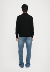 Pulover negru din tricot cu guler, asortat cu blugi lejeri de un albastru deschis. Materialul pare moale, cu o textură netedă și detalii minime.