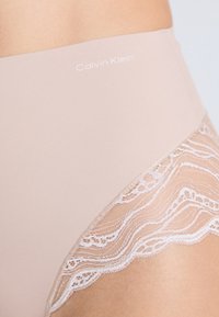 Nahé vysoké nohavičky s čipkovým lemovaním. Obsahuje mäkkú látku, logo Calvin Klein v bielej farbe a zložitú čipkovú dekoráciu na okrajoch.