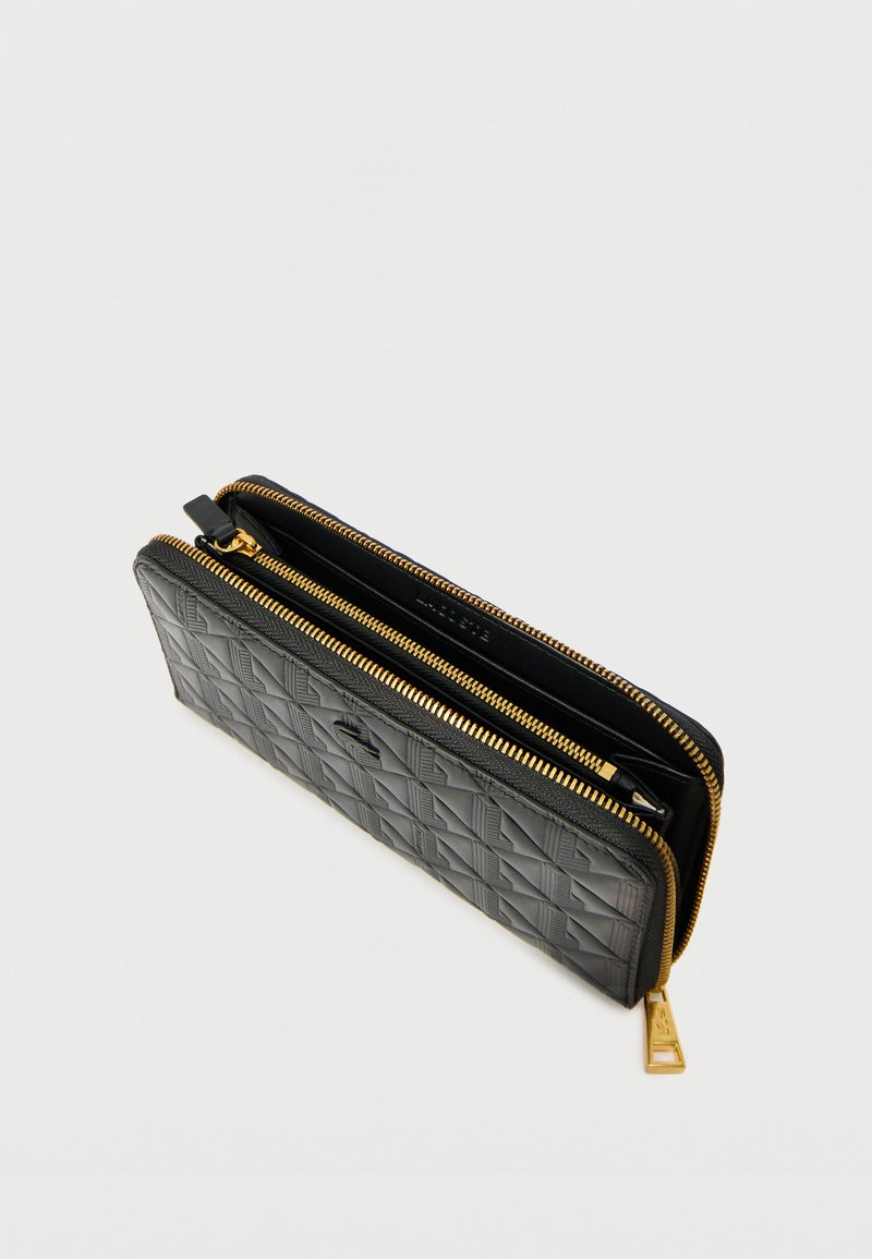 Zwarte gewatteerde portemonnee met gouden rits, met meerdere vakken en een getextureerde buitenkant. De ritssluiting heeft een klein metalen label.