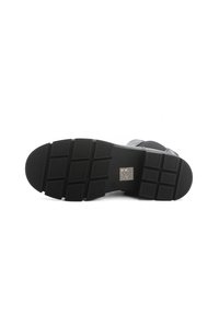 Suela de zapato de goma negra con un patrón de agarre texturizado, que presenta un diseño rectangular y detalles de marca en dorado en el centro.