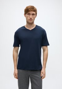 Μπλε ναυτικό κοντομάνικο T-shirt με V λαιμόκοψη από απαλό ύφασμα, συνδυασμένο με γκρι παντελόνι. Απλό σχέδιο χωρίς ορατά μοτίβα ή πρόσθετες λεπτομέρειες.