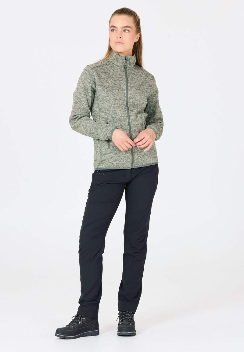 Grön texturerad zip-up jacka med ståkrage, kombinerad med svarta byxor. Skorna har svarta detaljer och robusta sula.